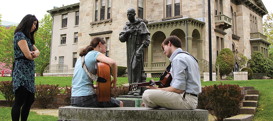 Students play guitar in front of a statue of Saint Martin de Porres on the campus of Providence College, Rhode Island.