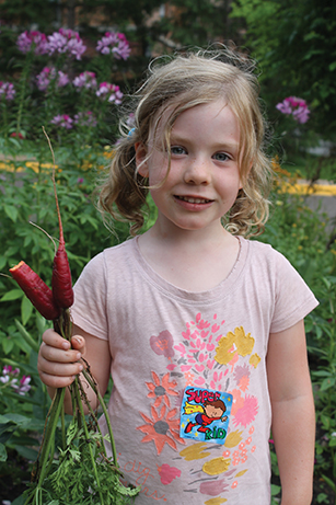 a little girl holds vegetables in Celeste’s Dream Community Garden 